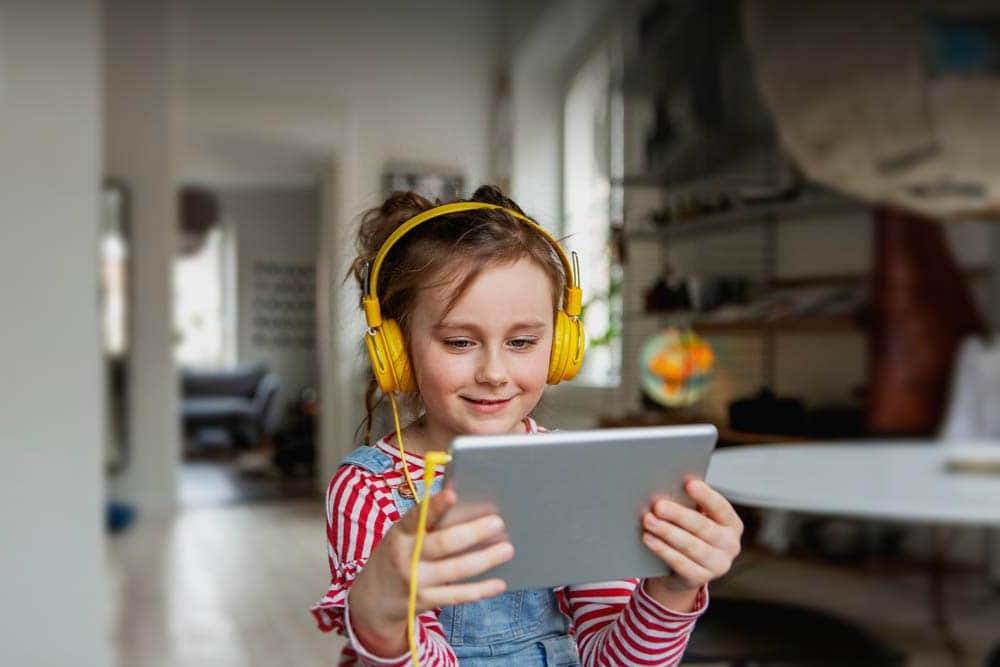 Young female student with a yellow headphones smiling looking at a laptop taking an online class at Iowa Connections Academy.